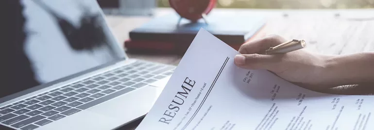 Person holding a resume in front of a laptop.