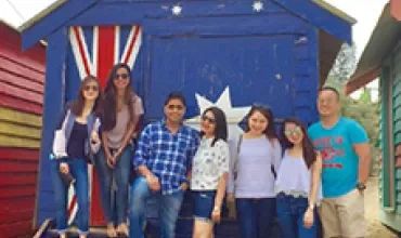 Group of people posing in front of a blue beach hut with Australian flag design.