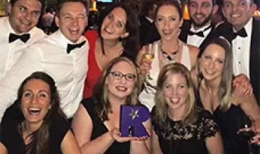 Group of people dressed formally at a celebration, smiling and holding a trophy.
