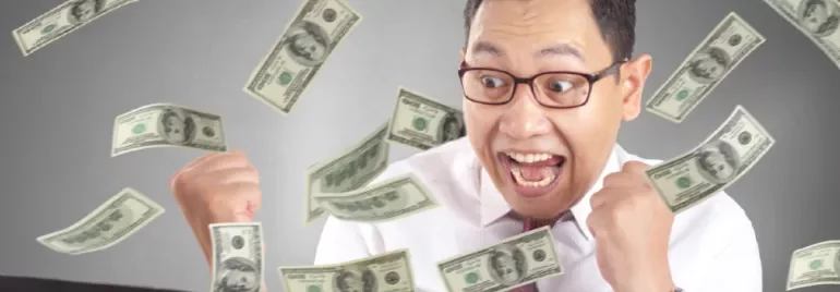 Man celebrating while dollar bills fly around him, looking excited at computer.