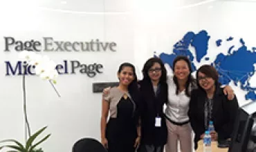 Four colleagues smiling in an office with 'Page Executive' sign, world map in the background.