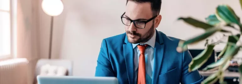 Man in blue suit working on a laptop in a modern office.